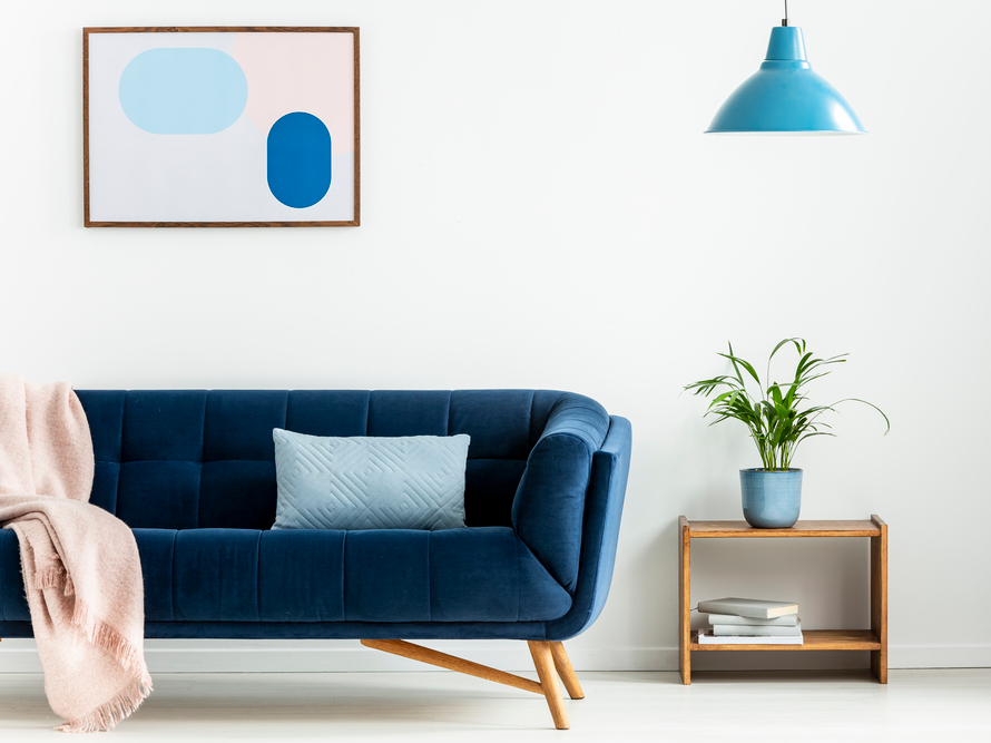 Pink blanket and blue pillow on couch in white flat interior with poster, plant and lamp. Real photo